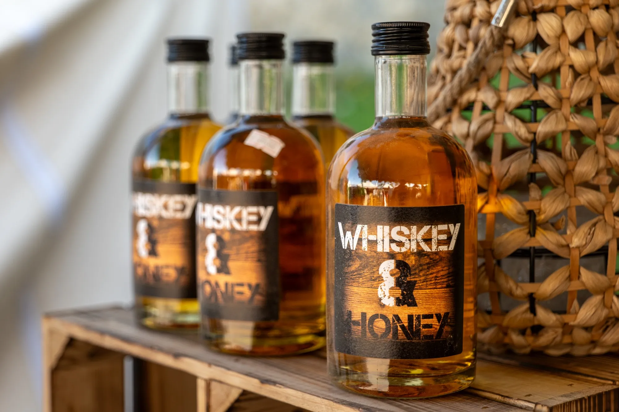 Flaschen Whiskey & Honey auf einer alten Holzkiste neben einem geflochtenen Korb